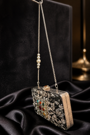 Luxury Meenakari filigree clutch bag with intricate floral metal detailing, colourful stone embellishments, and pearl chain sling design