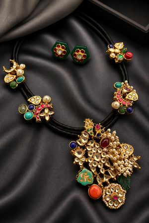 Black cord statement necklace with multicolor stones, jadau motifs, pearl detailing, and matching stud earrings in antique gold finish