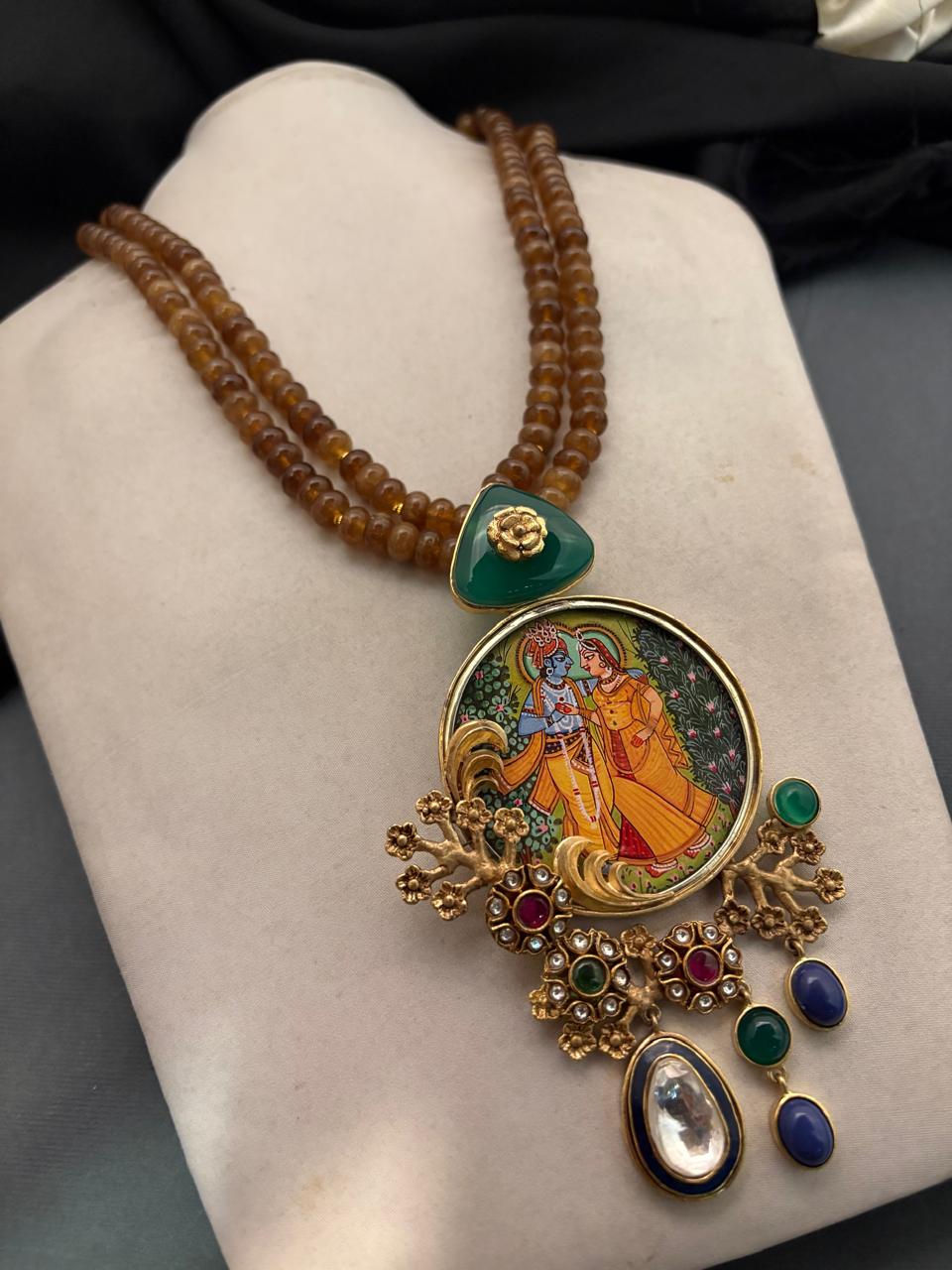 Miniature painting necklace with Radha Krishna artwork, kundan crystal detailing, and brown bead strands in traditional ethnic jewellery style