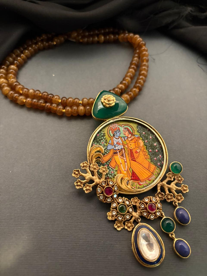 Miniature painting necklace with Radha Krishna artwork, kundan crystal detailing, and brown bead strands in traditional ethnic jewellery style