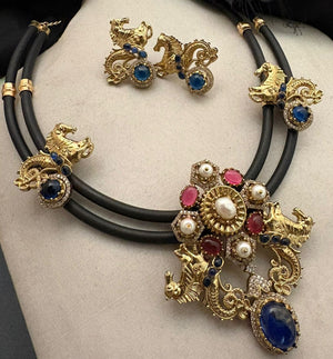 Antique gold horse motif necklace on black cord with blue and pink stones, pearl detailing, and matching designer earrings displayed on a jewellery bust