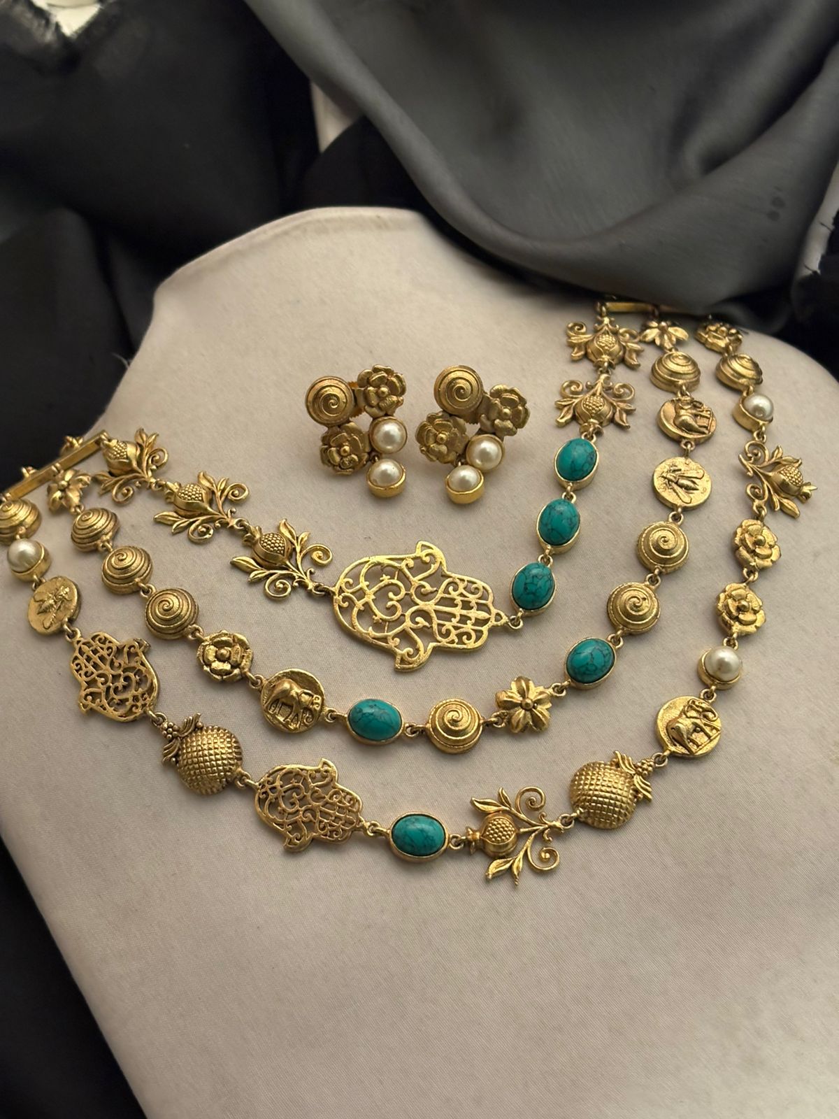 Antique gold layered necklace set with turquoise stones, floral motifs, heritage charms, and matching stud earrings displayed on a jewellery bust
