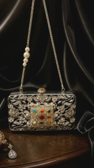 Luxury Meenakari filigree clutch bag with intricate floral metal detailing, colourful stone embellishments, and pearl chain sling design