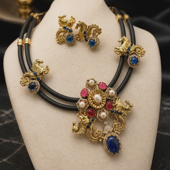 Antique gold horse motif necklace on black cord with blue and pink stones, pearl detailing, and matching designer earrings displayed on a jewellery bust