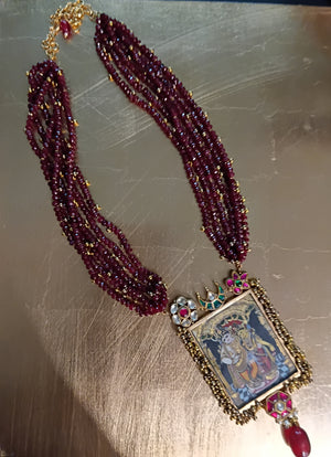 Decorative Radha Krishna necklace with maroon beads and a pendant on a reflective surface