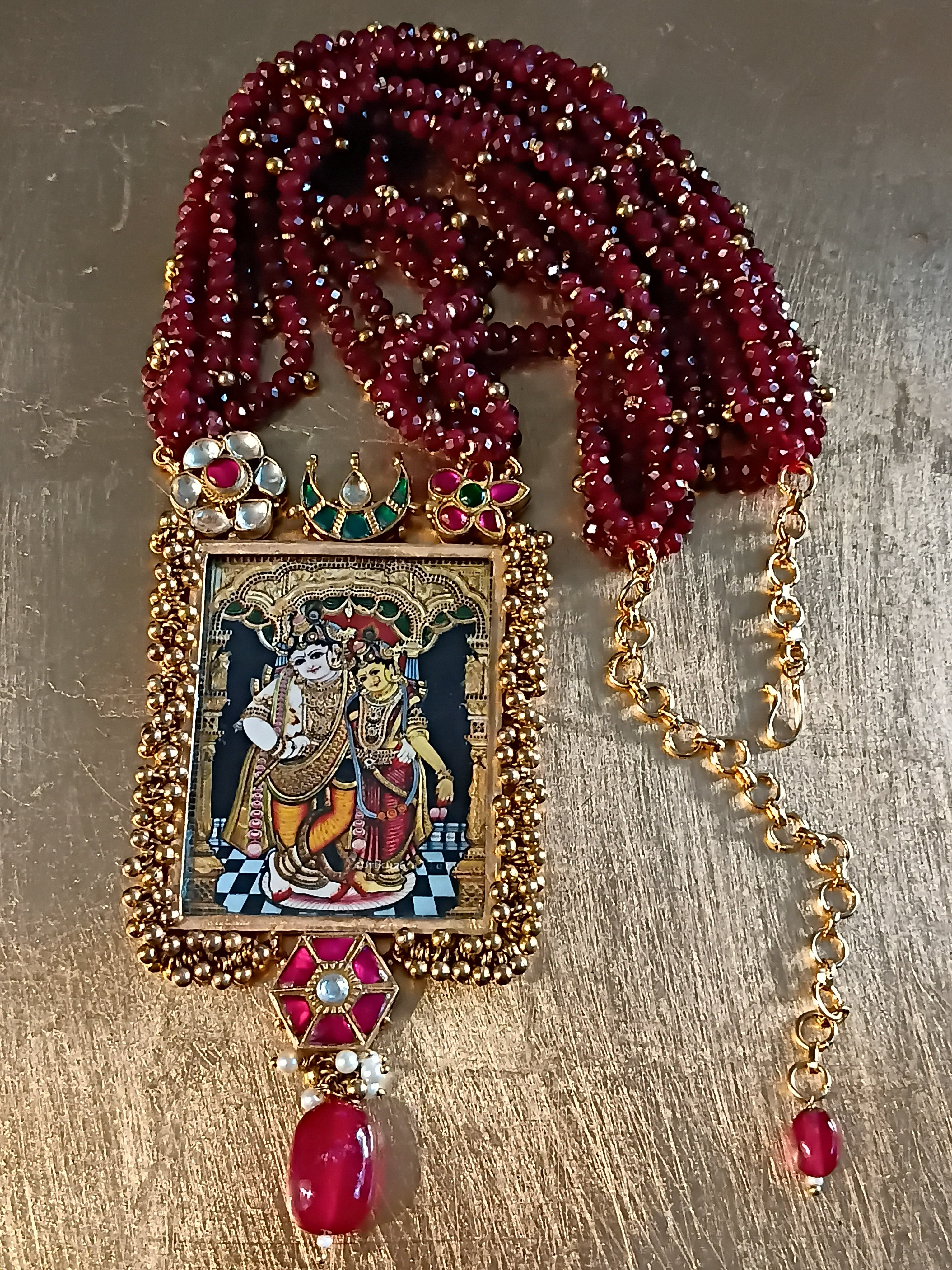 Decorative Radha Krishna necklace with ruby quartz beads and an ornate pendant on a metallic surface