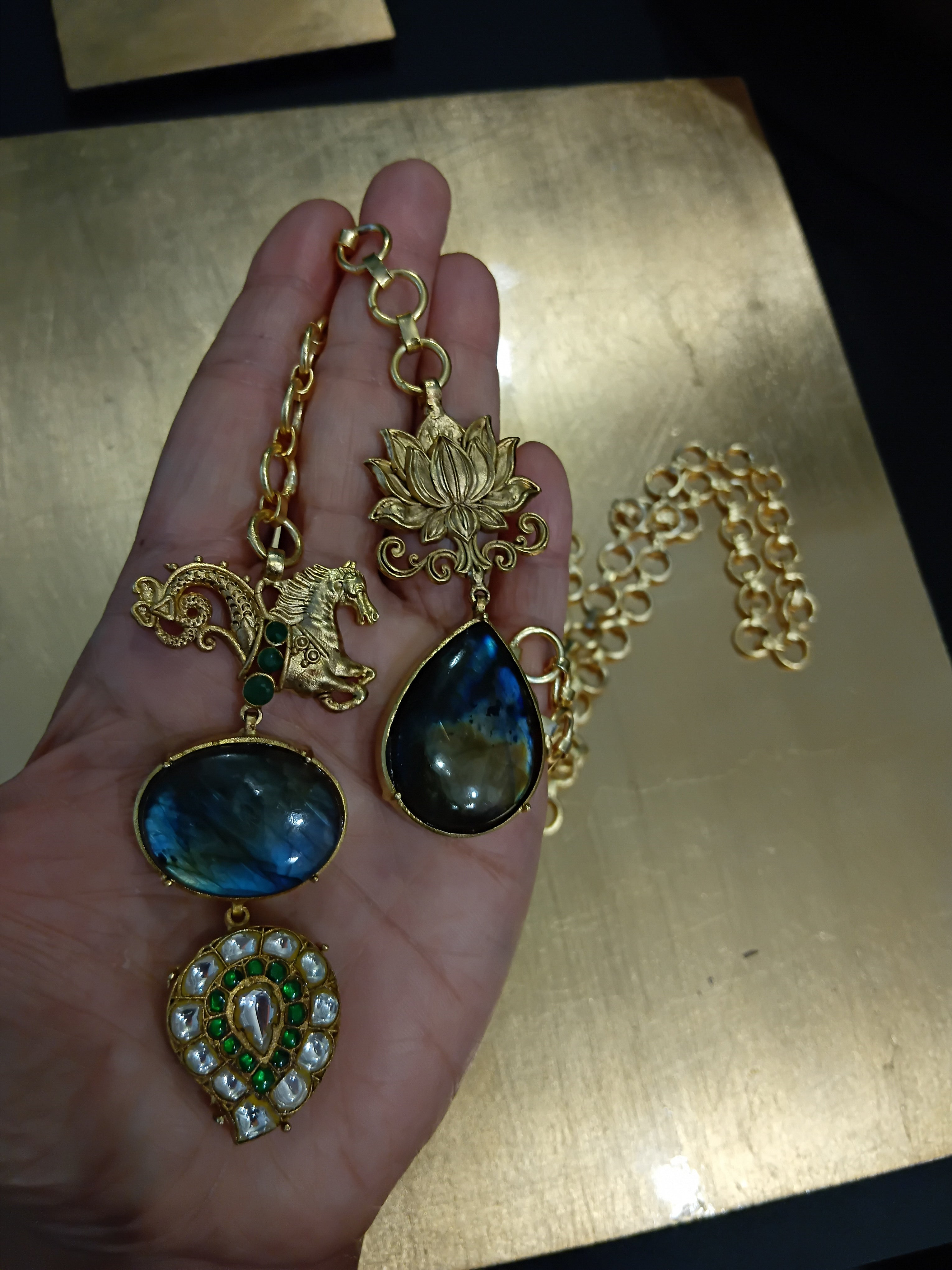 Hand holding gold necklaces with labradorite stones against a gold background